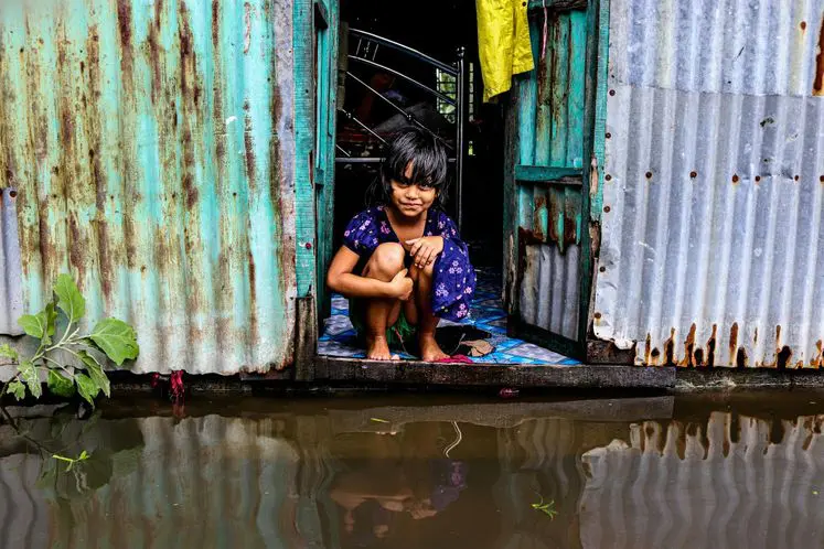 Girl sits in flooded shack doorway.