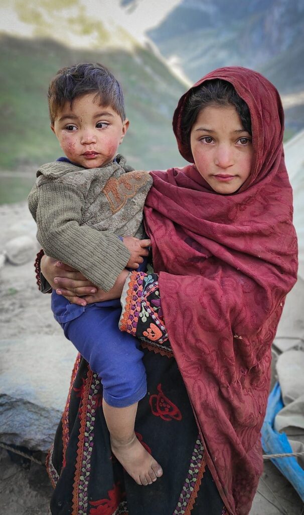 Girl holding young child in mountains.