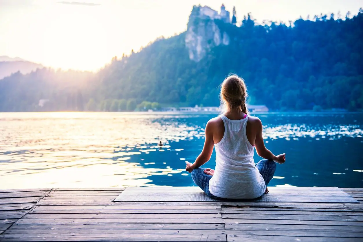 Woman meditating by peaceful lake.